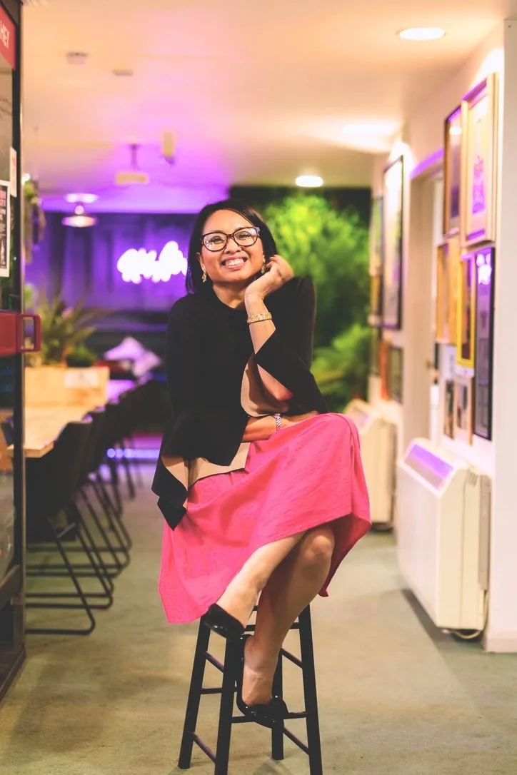 Rebecca Leppard seated on a bar stool in a pink skirt, smiling